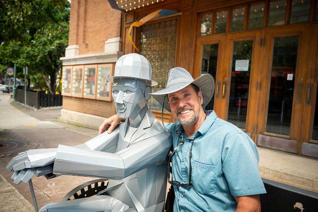 Eric assis à côté de la statue Charlie Chaplin, cinéma Princesse, Rivière-du-Loup